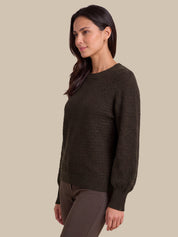 A woman wearing a dark brown textured knit sweater with long balloon sleeves, shown in a side profile against a solid beige background.