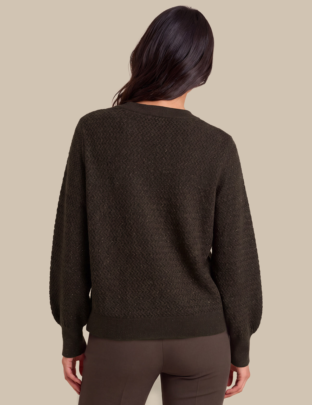 A woman viewed from the back wearing a dark brown textured knit sweater and matching dark brown pants against a solid beige background.
