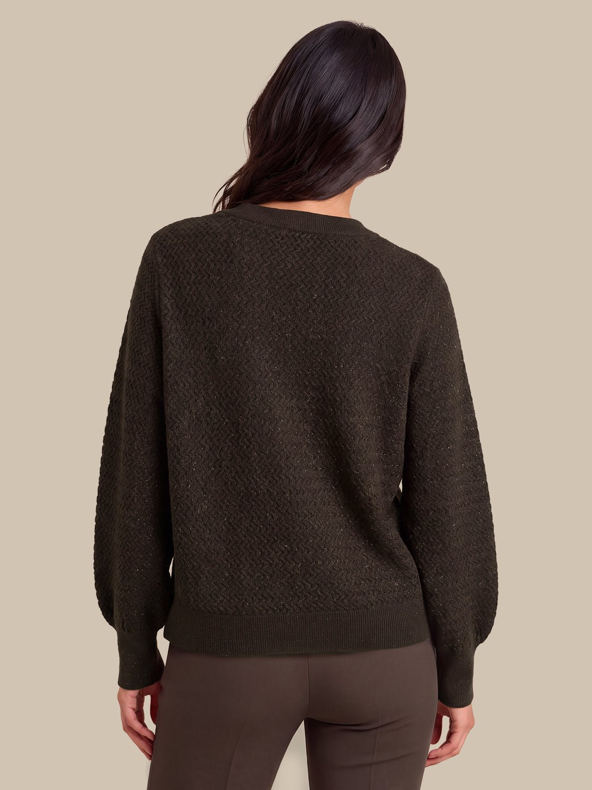 A woman viewed from the back wearing a dark brown textured knit sweater and matching dark brown pants against a solid beige background.