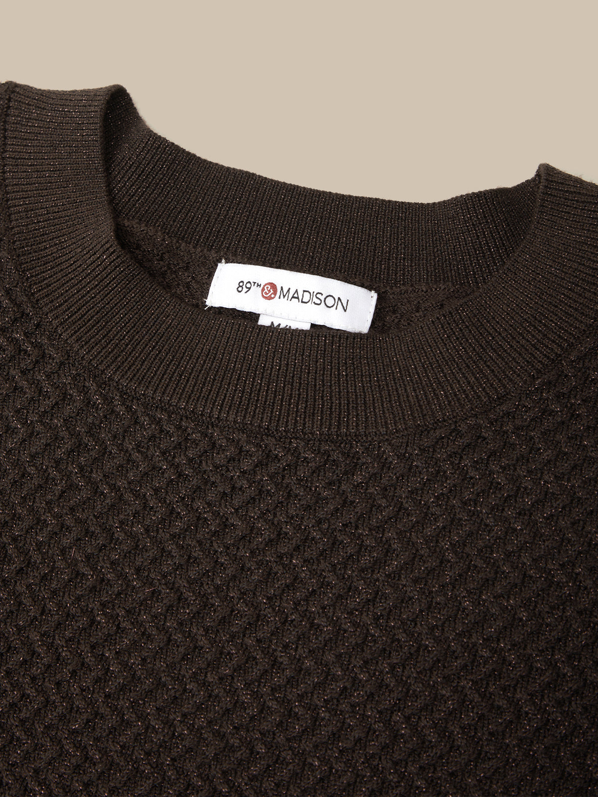 Close-up of a dark brown textured knit crewneck sweater with a white neck label reading '85% MADSON'.