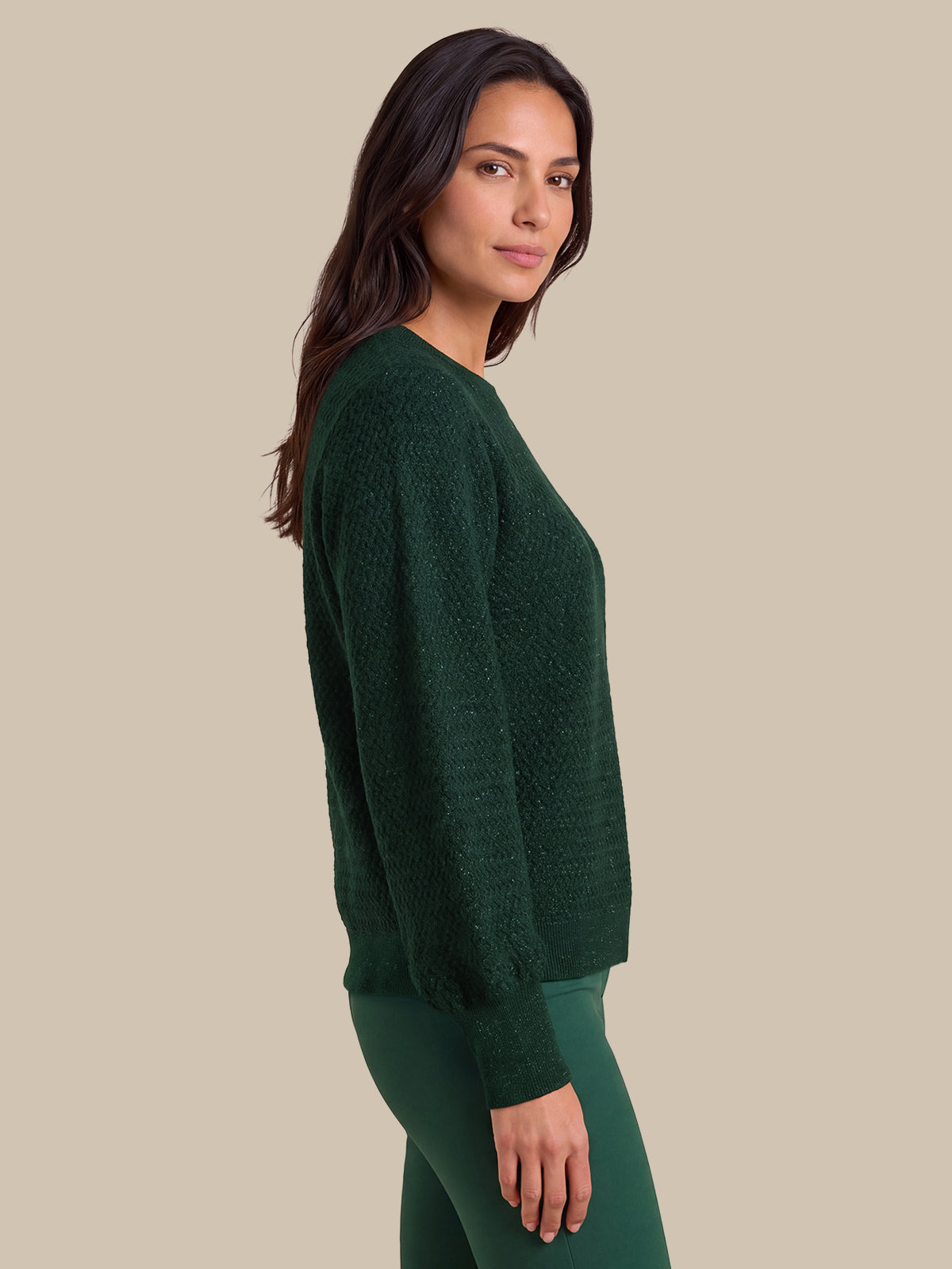 A woman shown in side profile wearing a dark green textured knit sweater and matching green leggings against a plain beige studio background.