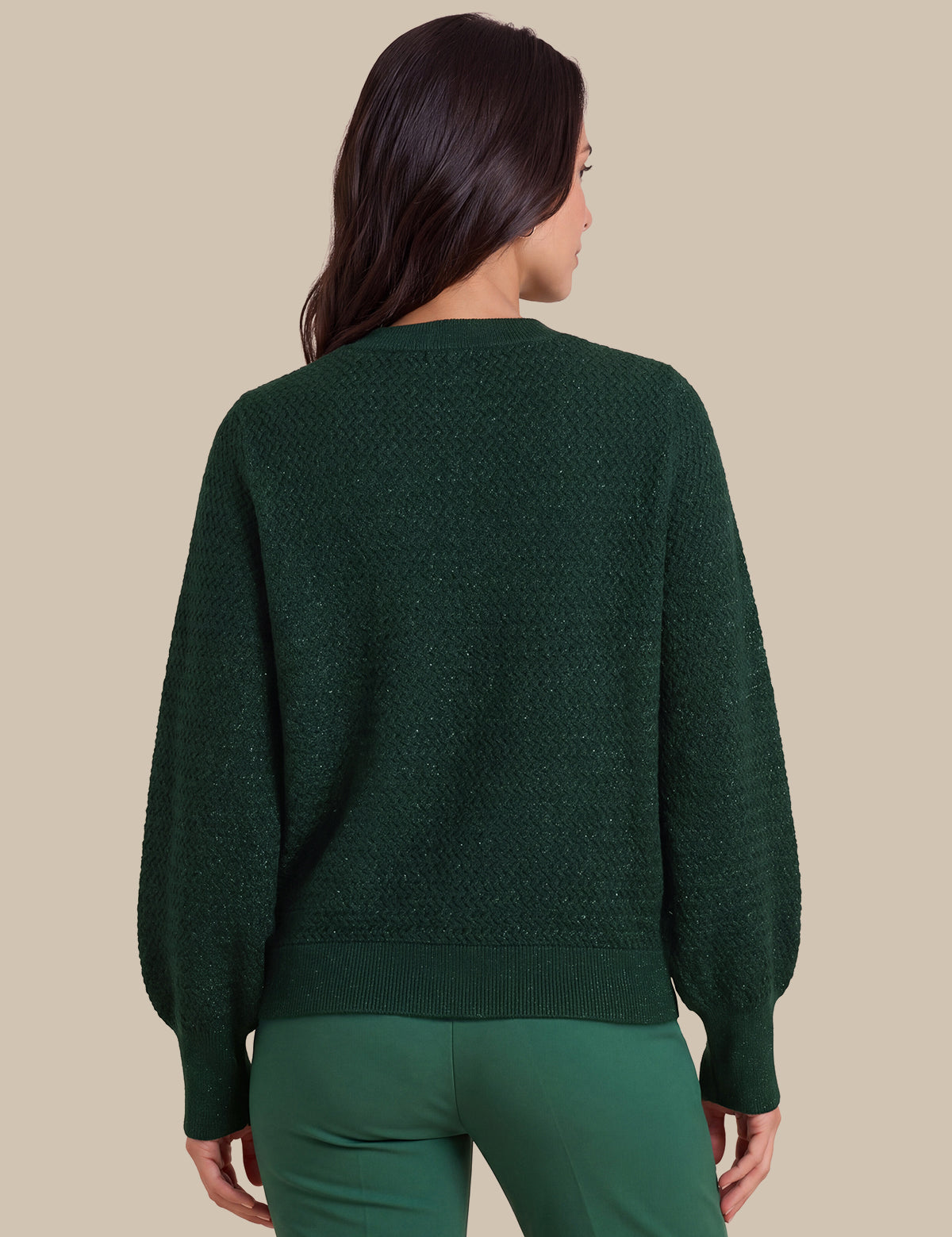 A woman shown from the back wearing a dark green textured knit sweater with balloon sleeves and matching green pants, set against a solid beige background.