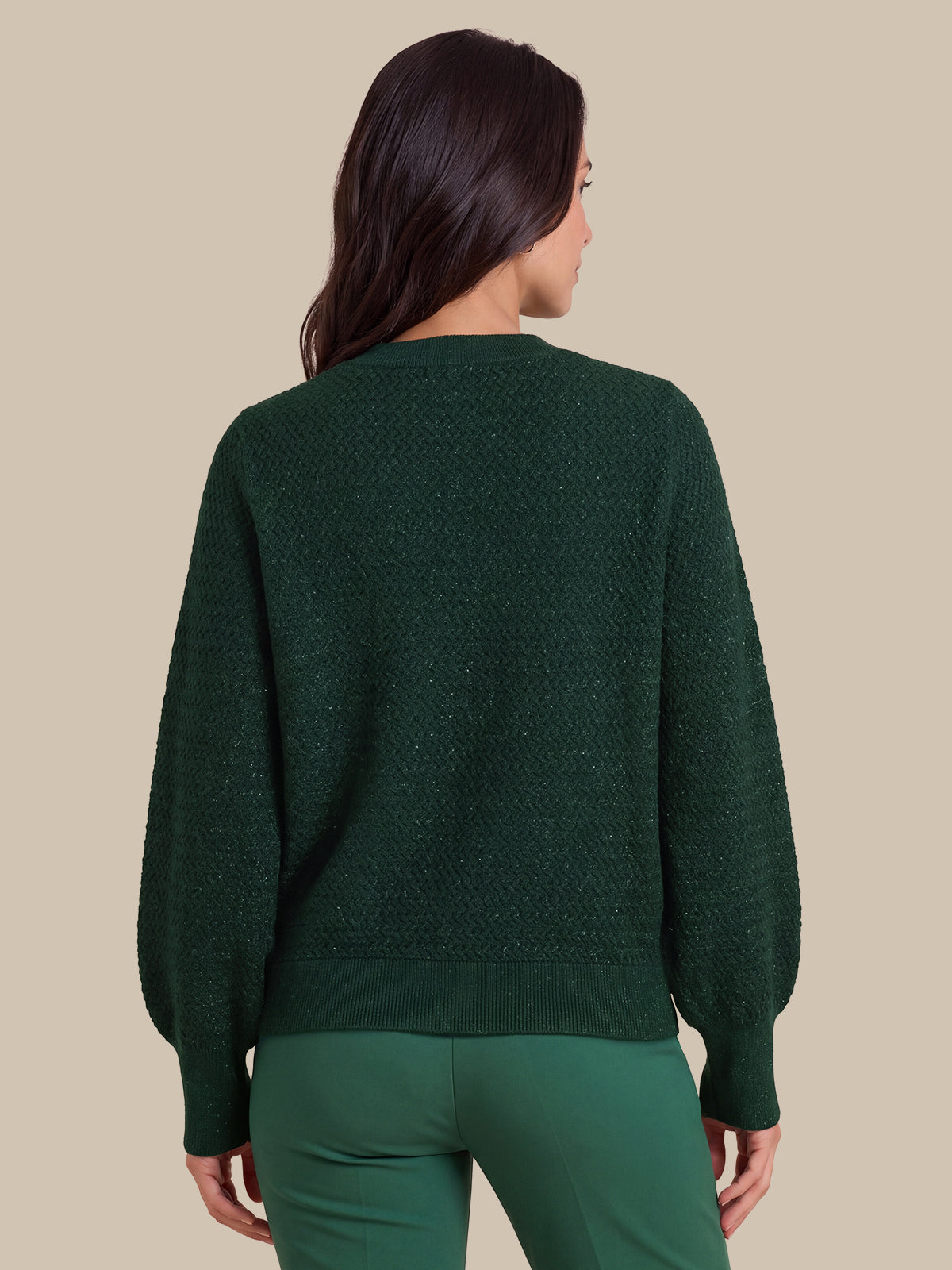 A woman shown from the back wearing a dark green textured knit sweater with balloon sleeves and matching green pants, set against a solid beige background.