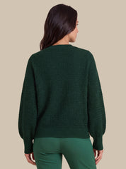 A woman shown from the back wearing a dark green textured knit sweater with balloon sleeves and matching green pants, set against a solid beige background.