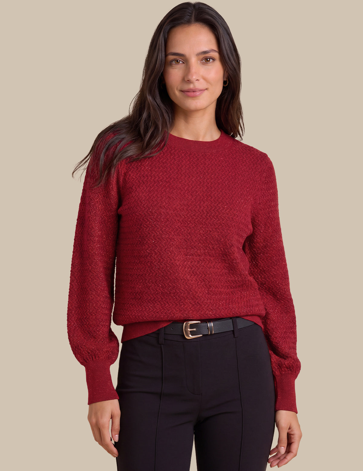 A woman wearing a textured crewneck sweater in deep burgundy red, paired with black trousers and a black belt, against a solid beige background.