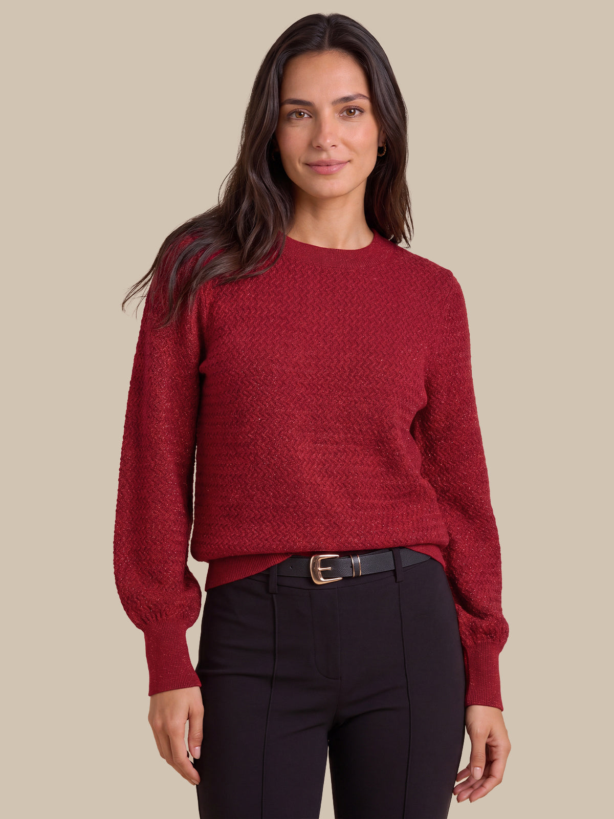A woman wearing a textured crewneck sweater in deep burgundy red, paired with black trousers and a black belt, against a solid beige background.