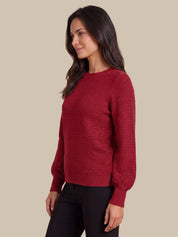 A woman wearing a textured, deep red crewneck sweater and black pants, shown in a side-profile view against a solid beige background.