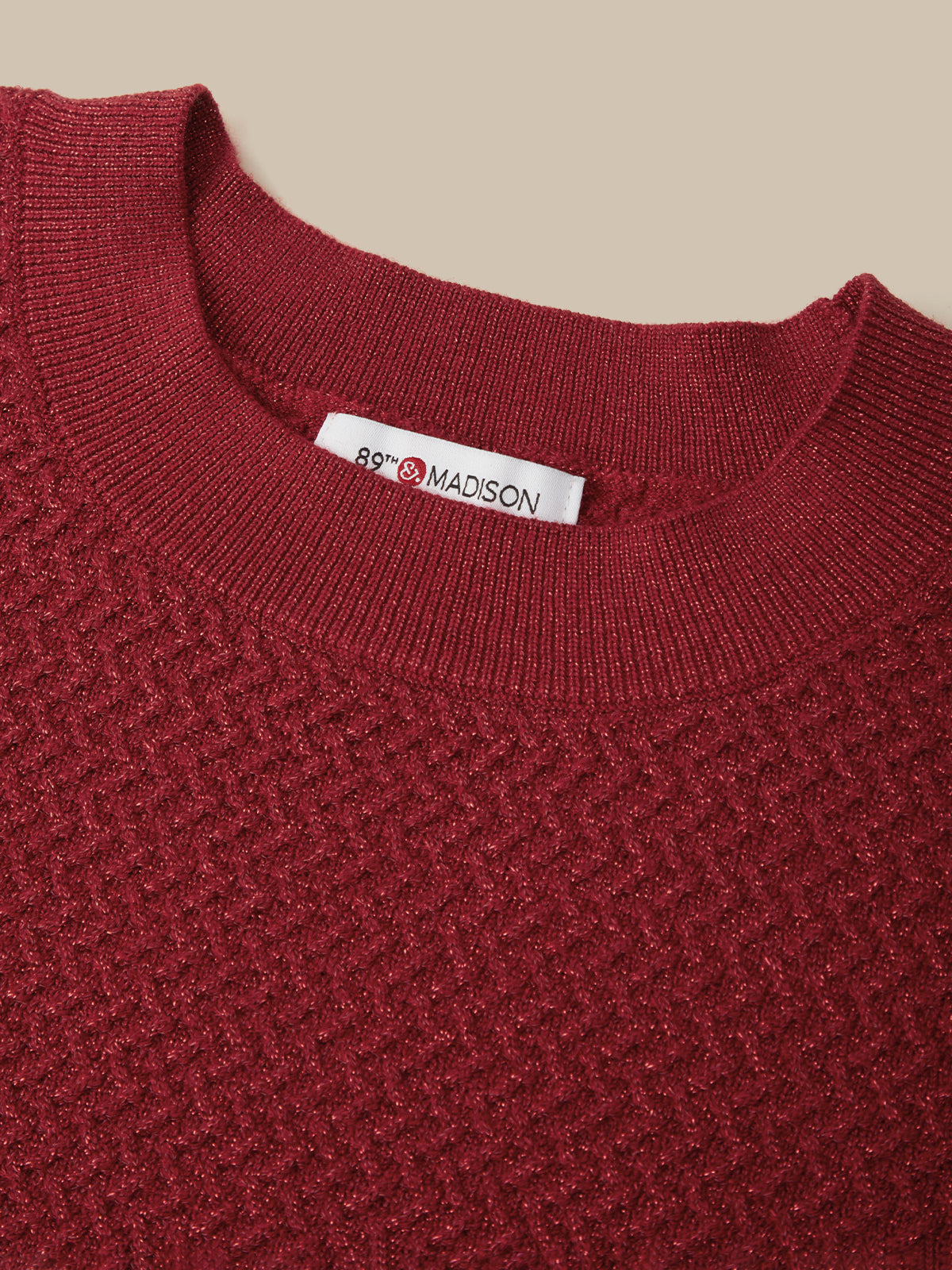 Close-up of a textured knit crewneck sweater in deep burgundy red, showing a white neck label with the brand name '88th & MADISON'.