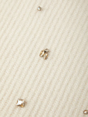 Close-up of a ribbed cream knit fabric with several small clear rhinestone studs and clusters scattered across the surface.