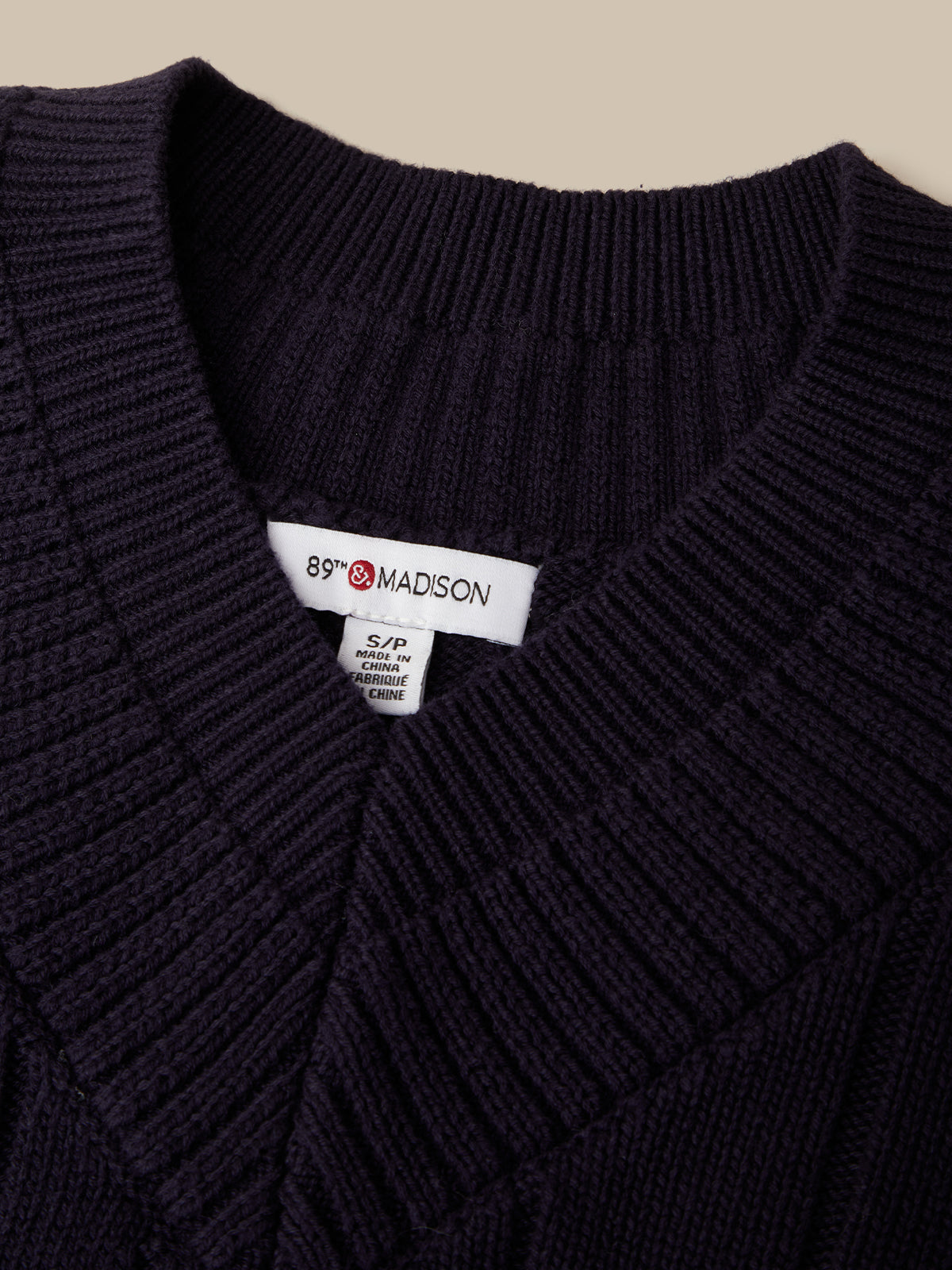 Close-up of a dark navy ribbed knit sweater with a white neck label reading 89 MADISON.