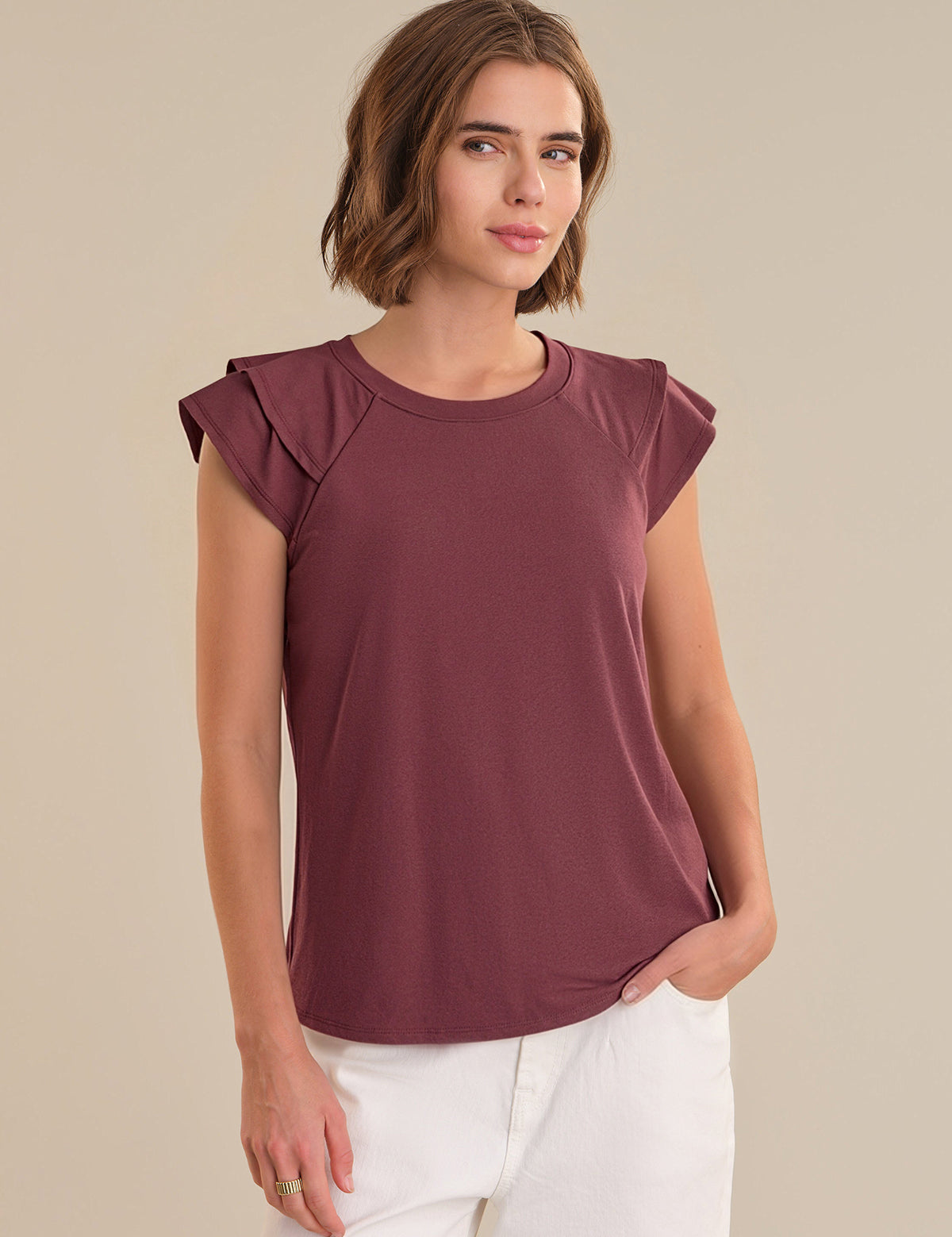 Woman wearing a maroon top with ruffled shoulders against a beige background
