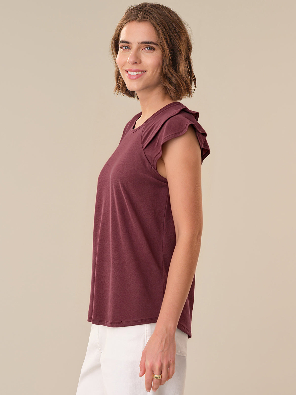 Woman wearing a maroon sleeveless top with ruffled shoulders against a beige background
