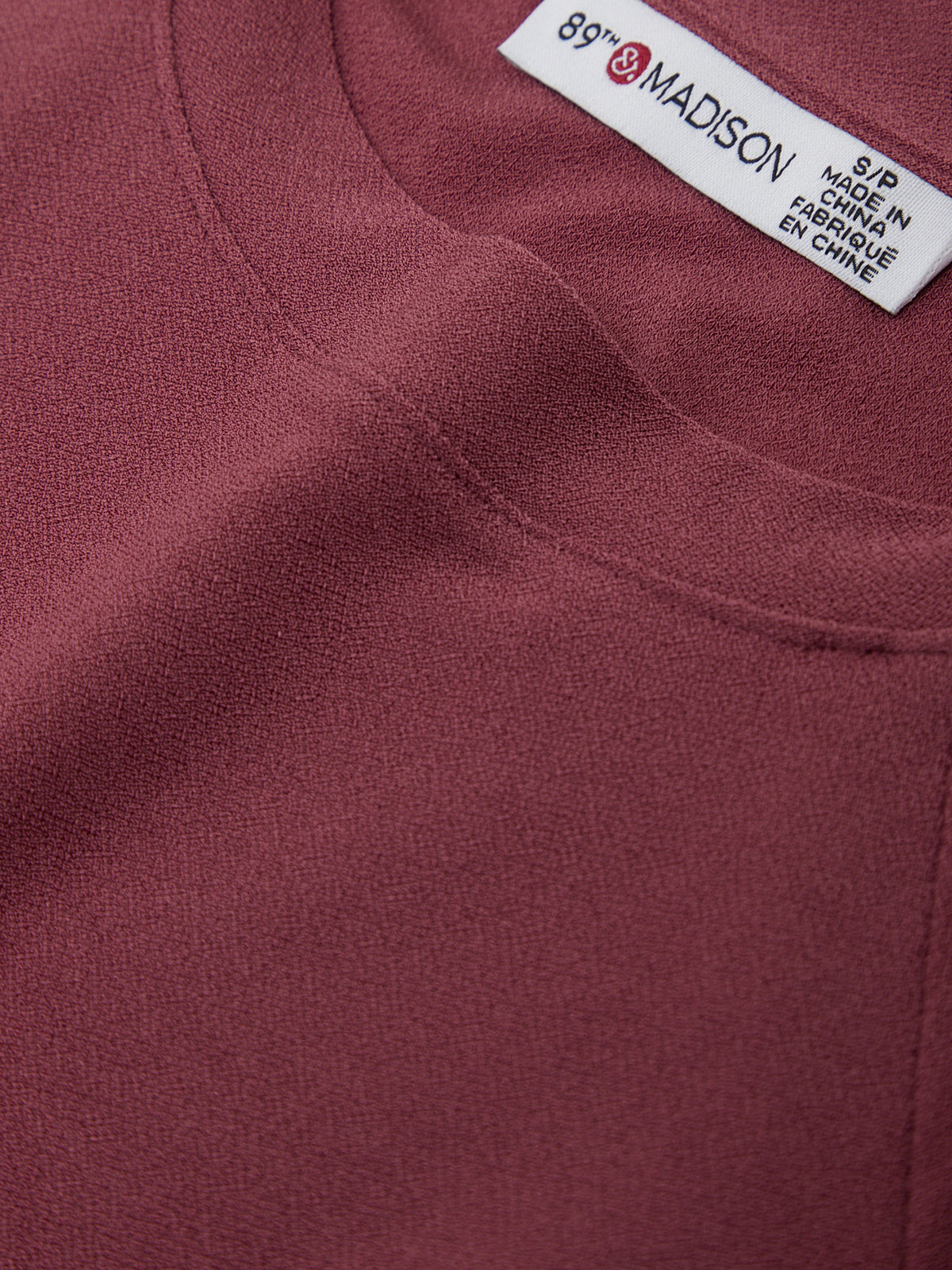 Close-up of a maroon garment with a label on a white background