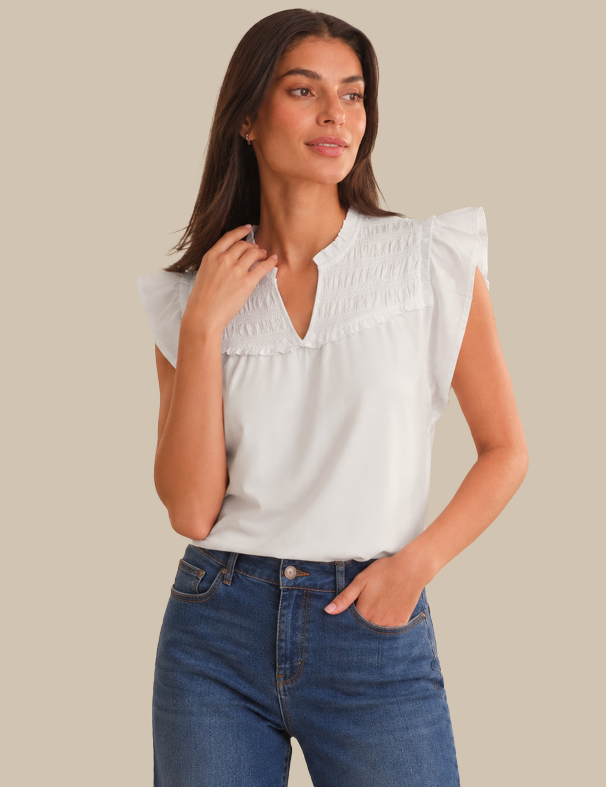 Woman wearing a white blouse with ruffled shoulders and blue jeans on a beige background