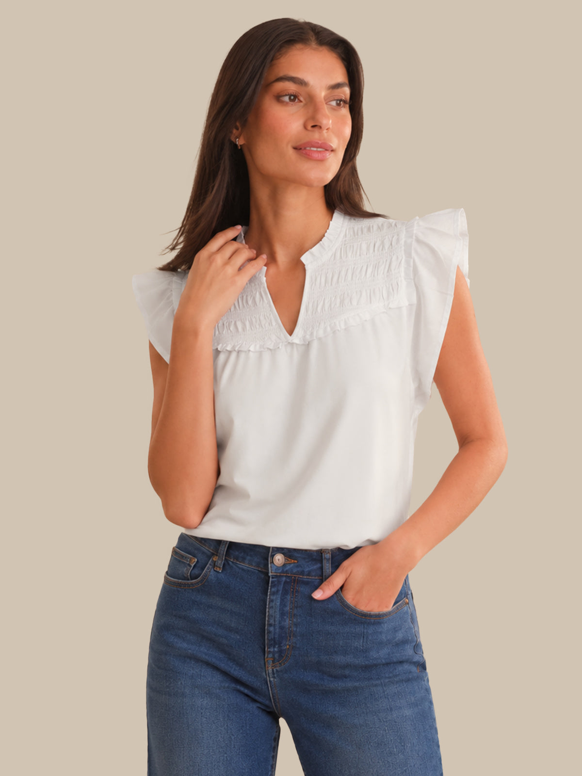 Woman wearing a white blouse with ruffled shoulders and blue jeans on a beige background