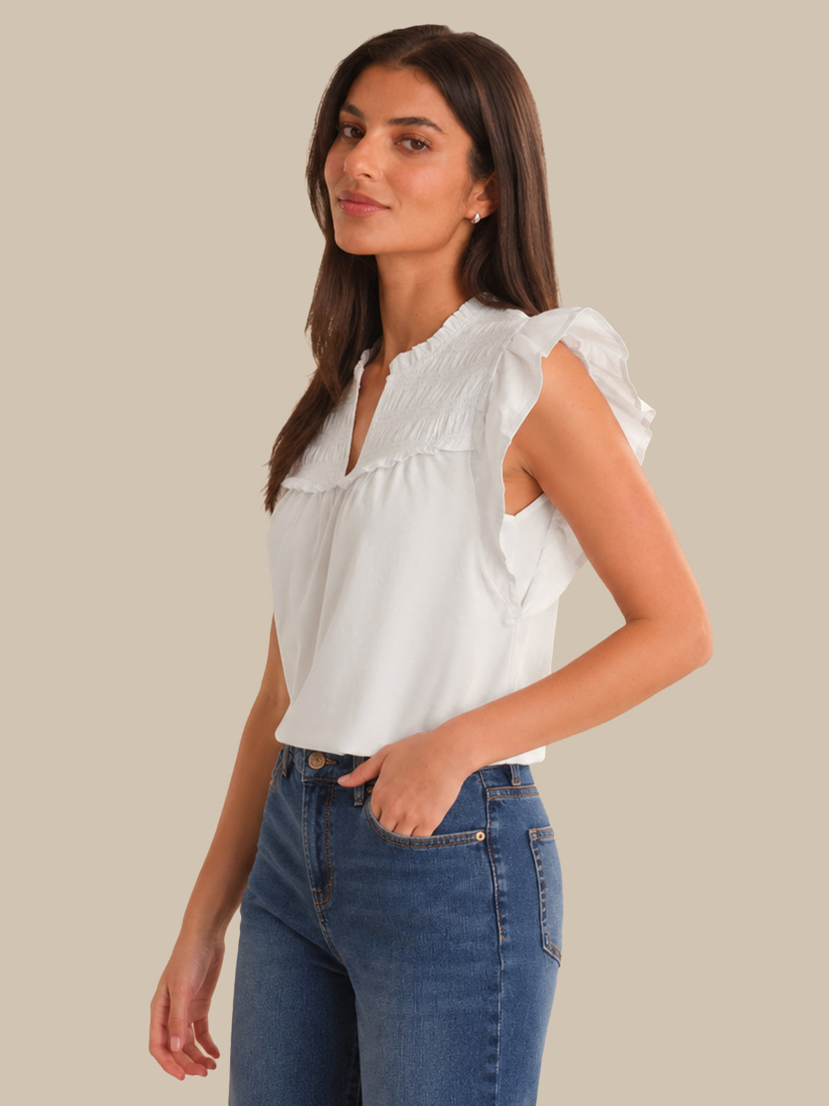 Woman wearing a white blouse with ruffled sleeves and blue jeans on a beige background