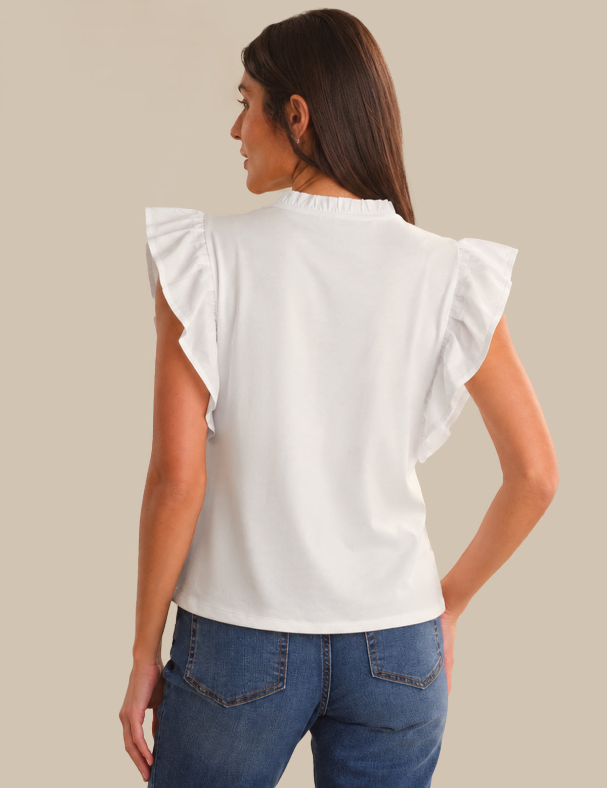 Woman wearing a white top with ruffled sleeves and blue jeans on a beige background