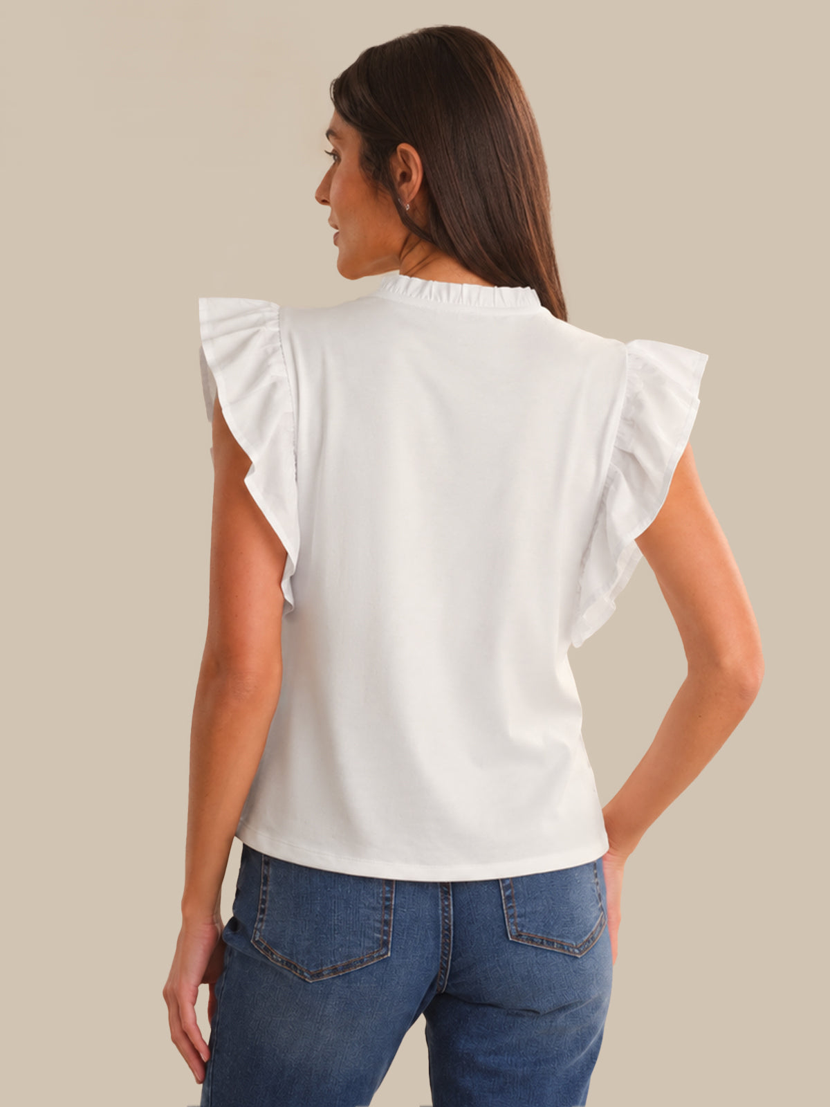 Woman wearing a white top with ruffled sleeves and blue jeans on a beige background