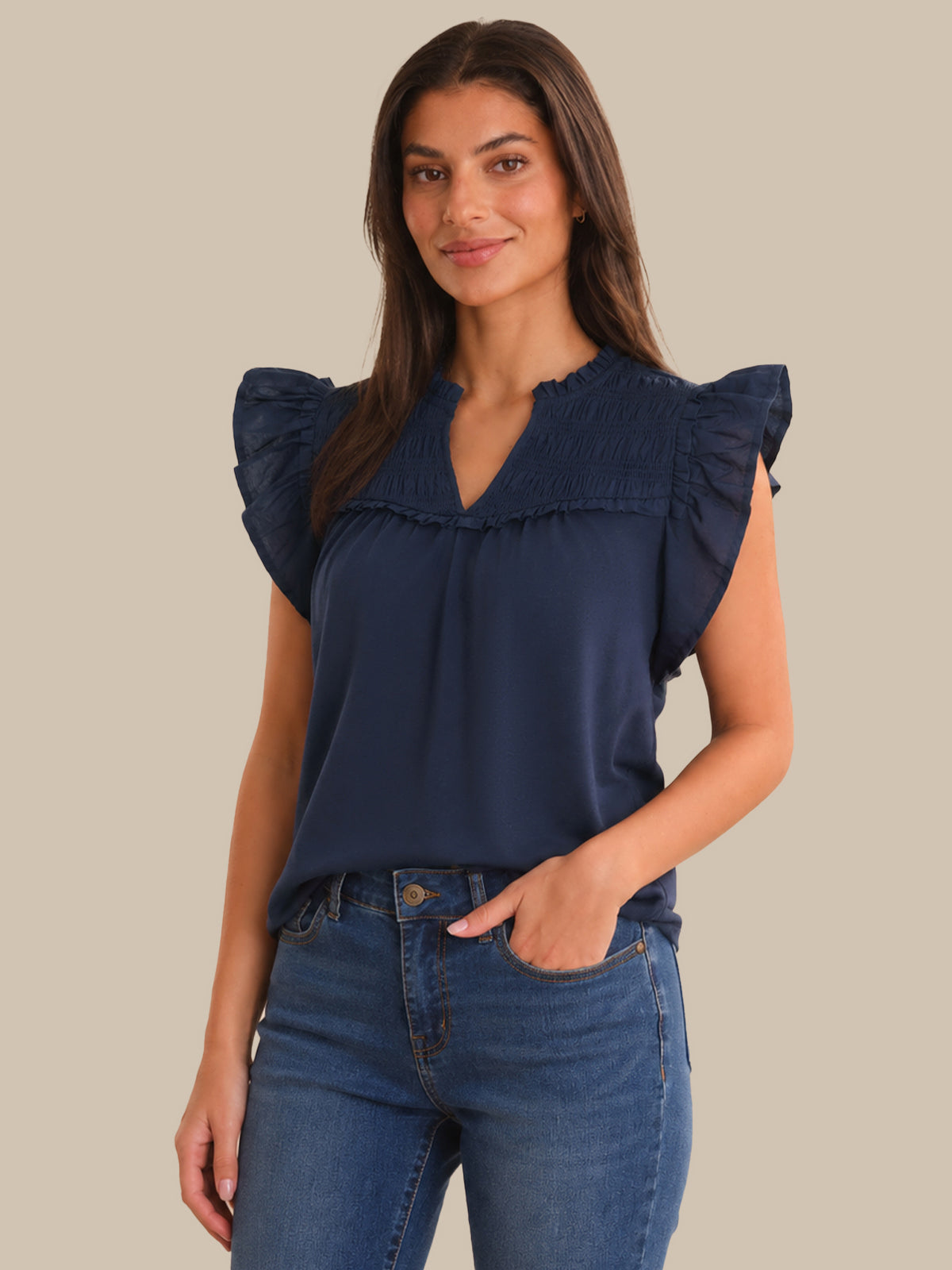 Woman wearing a navy blue top with ruffled sleeves against a beige background