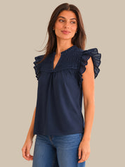 Woman wearing a navy blue blouse with ruffled shoulders against a neutral background