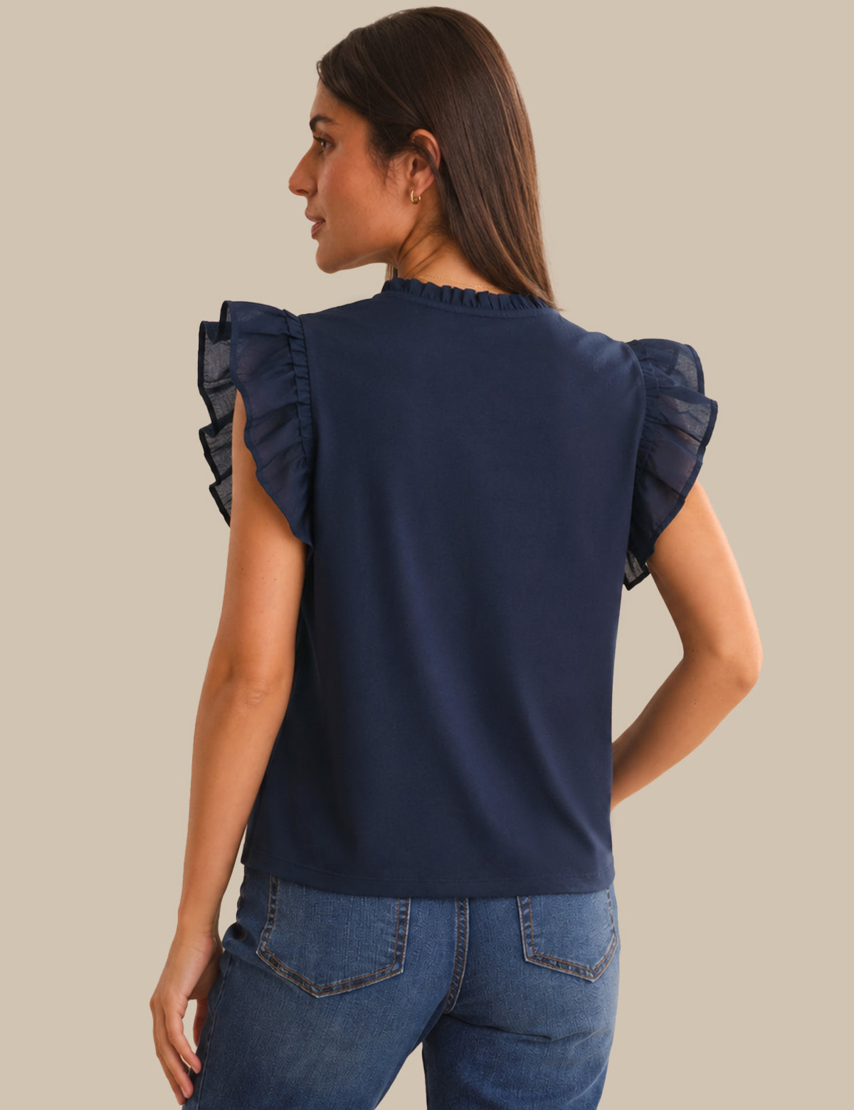 Woman wearing a navy blue top with ruffled shoulders on a beige background