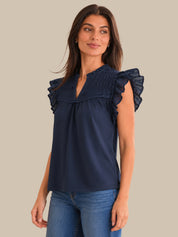 Woman wearing a navy blue blouse with ruffled shoulders against a beige background