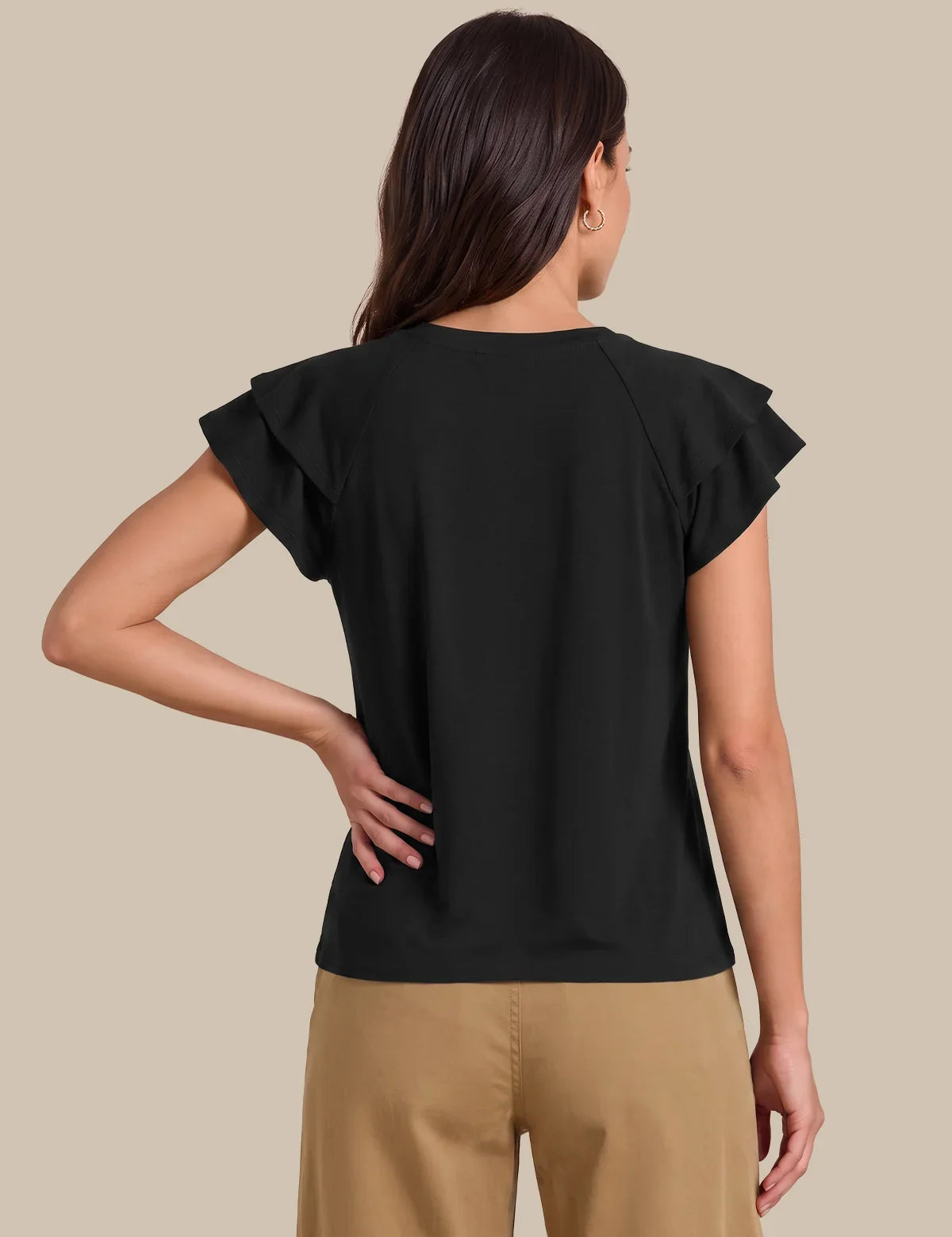 A woman shown from the back wearing a black short-sleeve top with ruffled edges and tan pants, against a plain beige studio background.