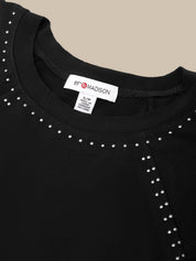 Close-up of a black crewneck top with silver stud embellishments around the neckline, showing a white brand label that reads 69& MADISON.