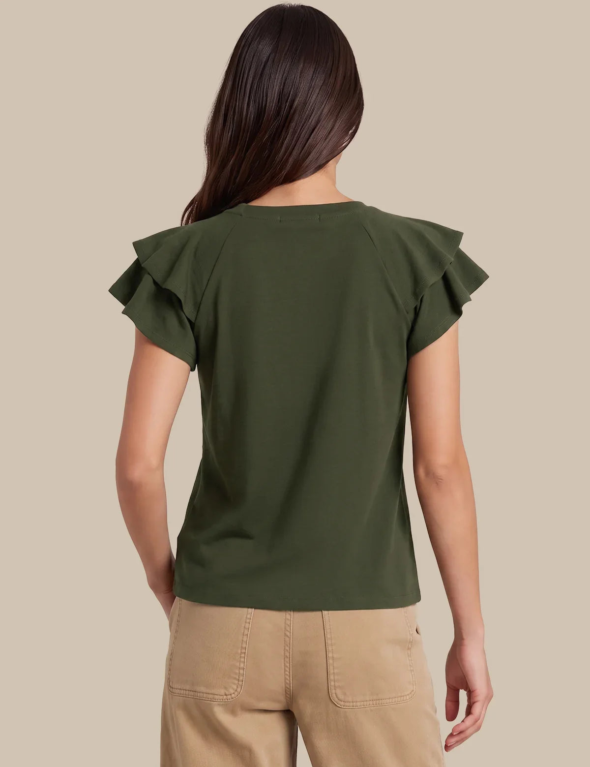 A woman shown from the back wearing an olive green short-sleeve top with ruffled shoulder details and beige pants, set against a solid beige background.