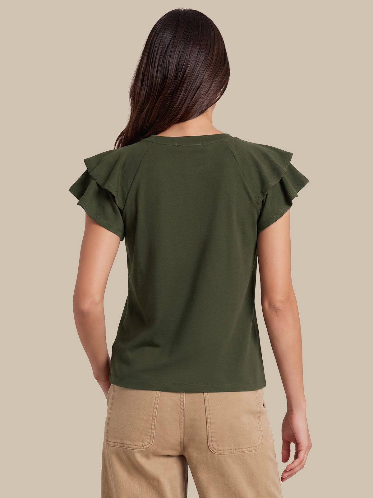 A woman shown from the back wearing an olive green short-sleeve top with ruffled shoulder details and beige pants, set against a solid beige background.