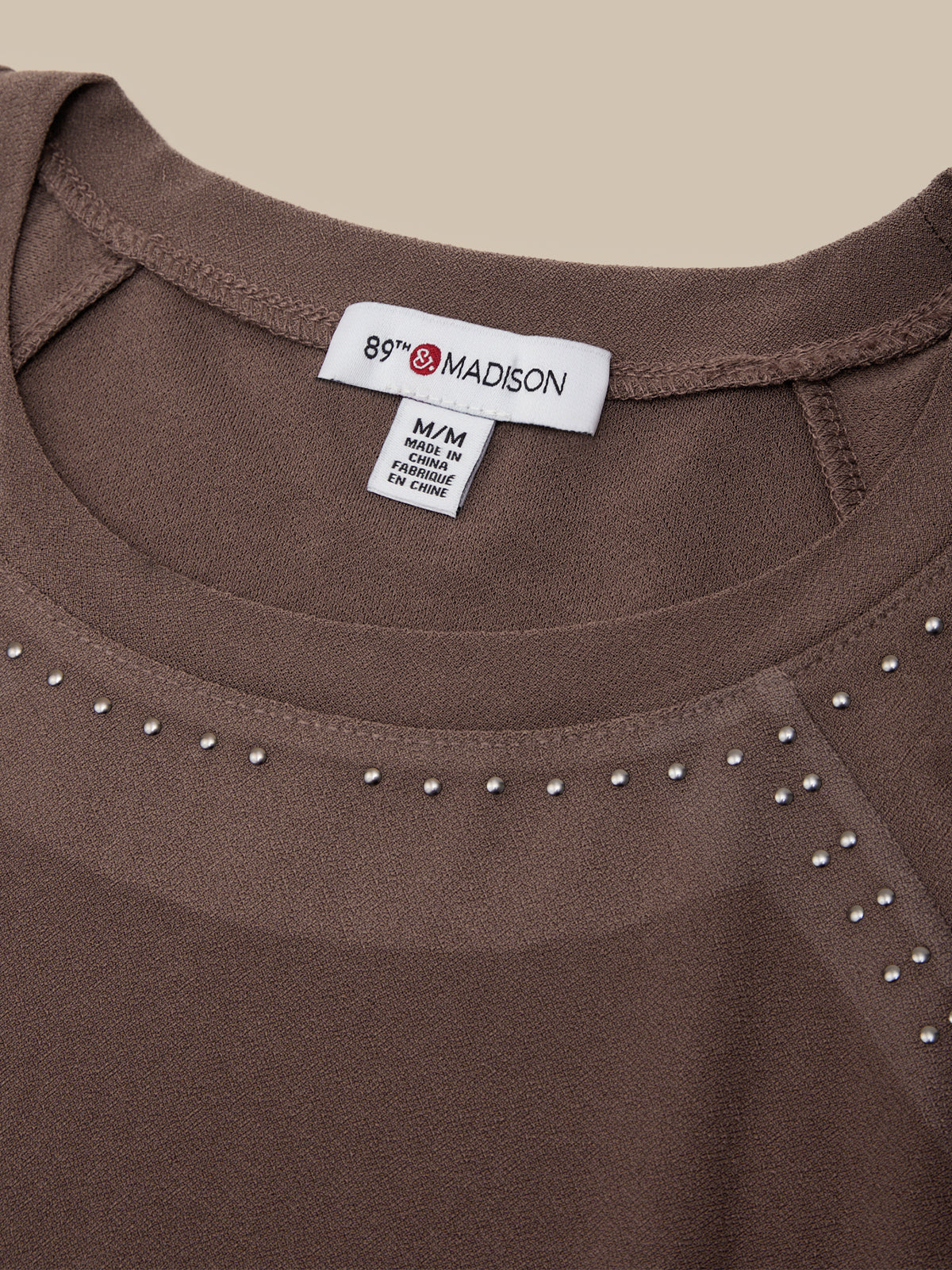 Close-up of a brown scoop-neck top with silver rhinestone trim along the neckline, showing the 89th & Madison brand label.