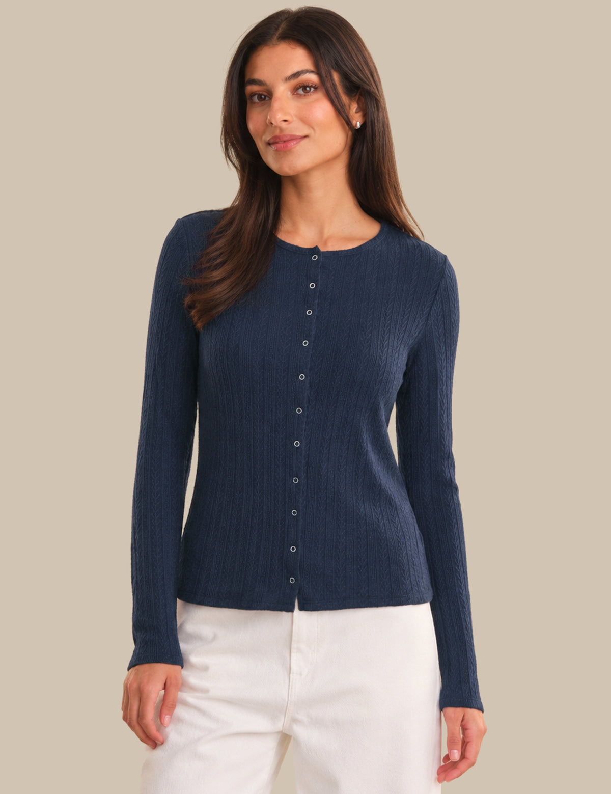 Woman wearing a navy blue ribbed cardigan with buttons on a beige background