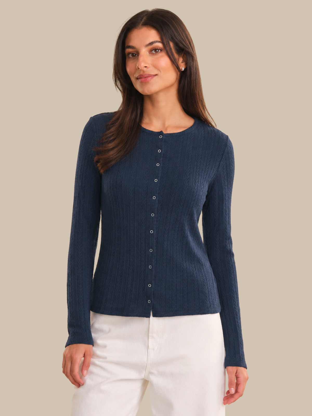 Woman wearing a navy blue ribbed cardigan with buttons on a beige background