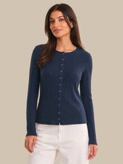 Woman wearing a navy blue ribbed cardigan with buttons on a beige background