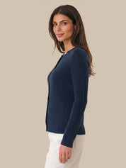 Woman wearing a navy blue ribbed cardigan and white pants on a beige background