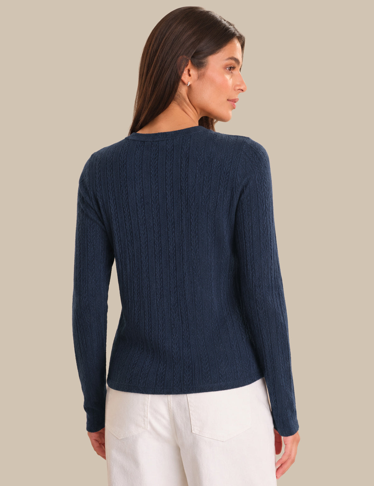 Woman wearing a navy blue cardigan and white pants against a beige background