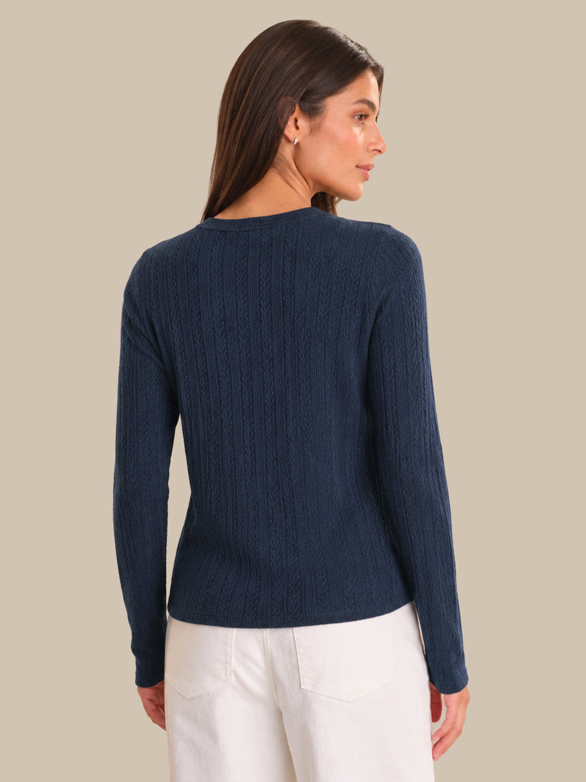 Woman wearing a navy blue cardigan and white pants against a beige background