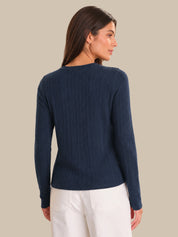 Woman wearing a navy blue cardigan and white pants against a beige background