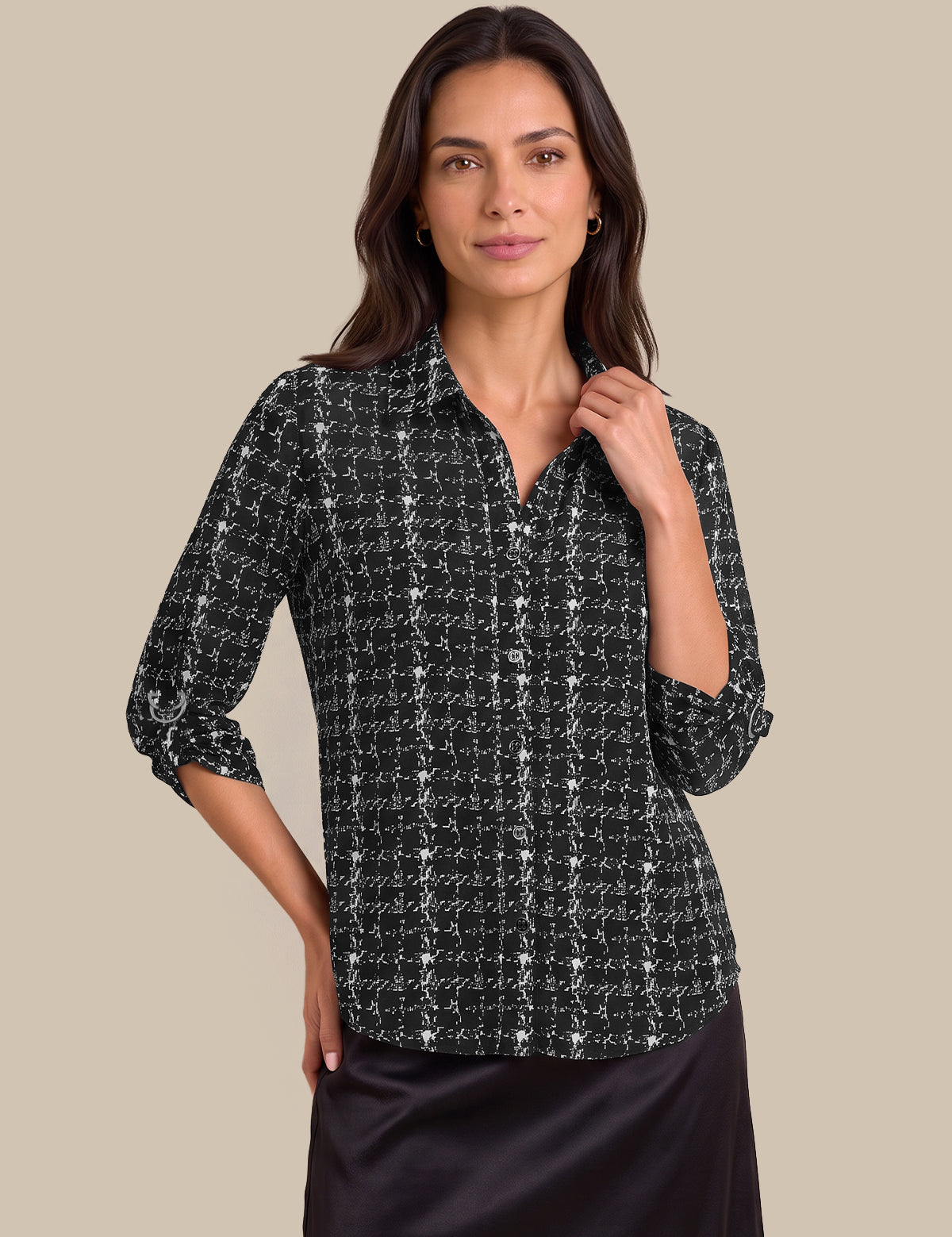 A woman modeling a black and white tweed button-down shirt with three-quarter sleeves, paired with a black satin skirt, against a solid beige background.