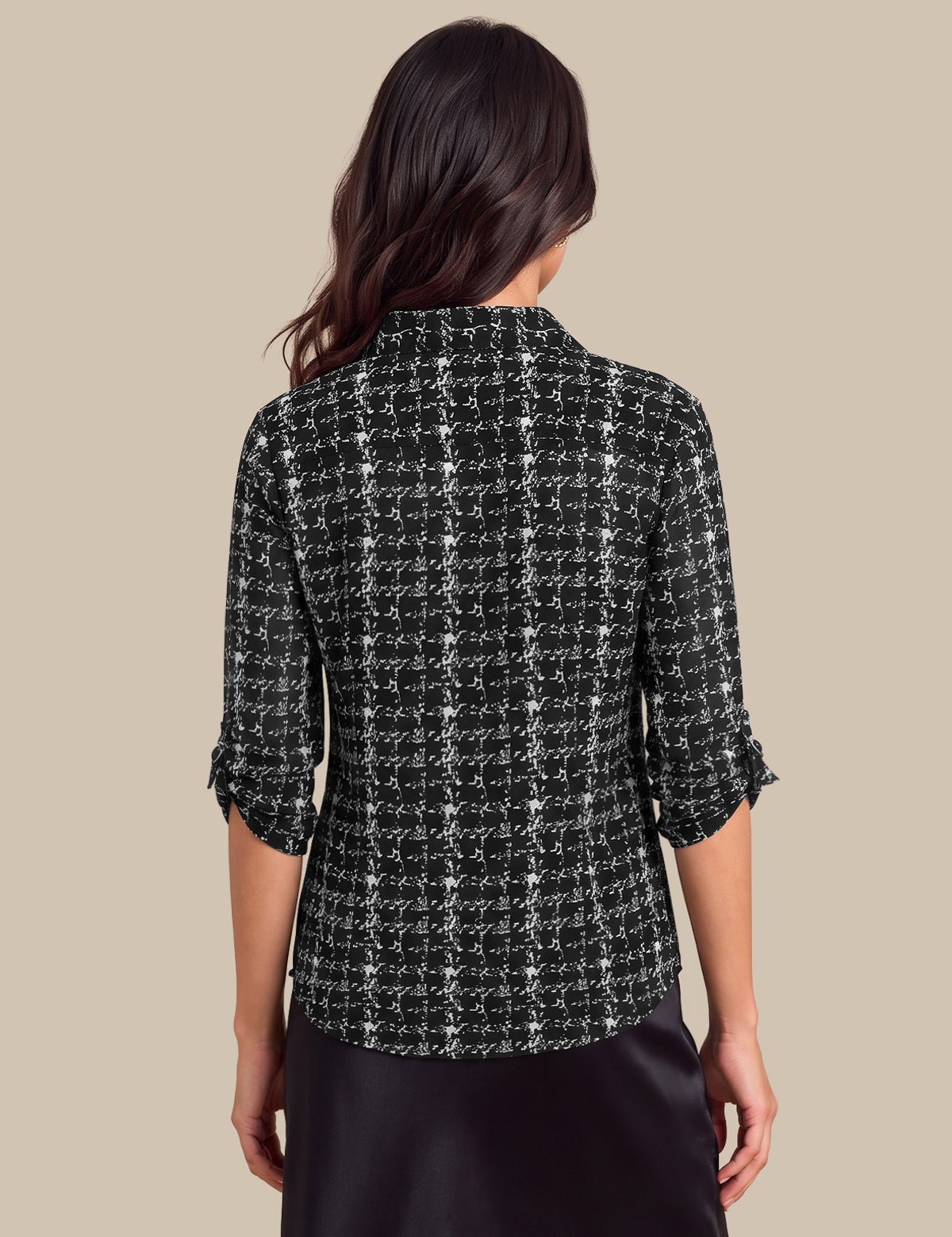 A woman shown from the back wearing a black and white tweed plaid shirt with three-quarter sleeves and a dark skirt, set against a solid beige background.