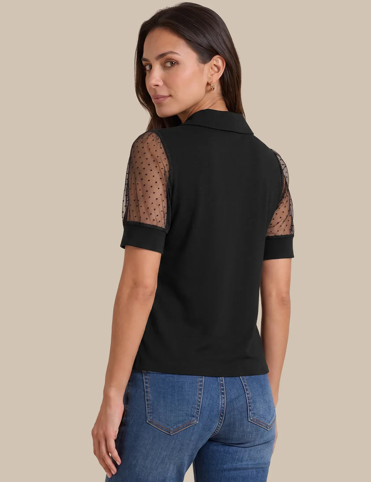 A woman shown from the back wearing a black short-sleeve polo shirt with sheer polka-dot mesh sleeves, paired with blue jeans, against a solid beige background.