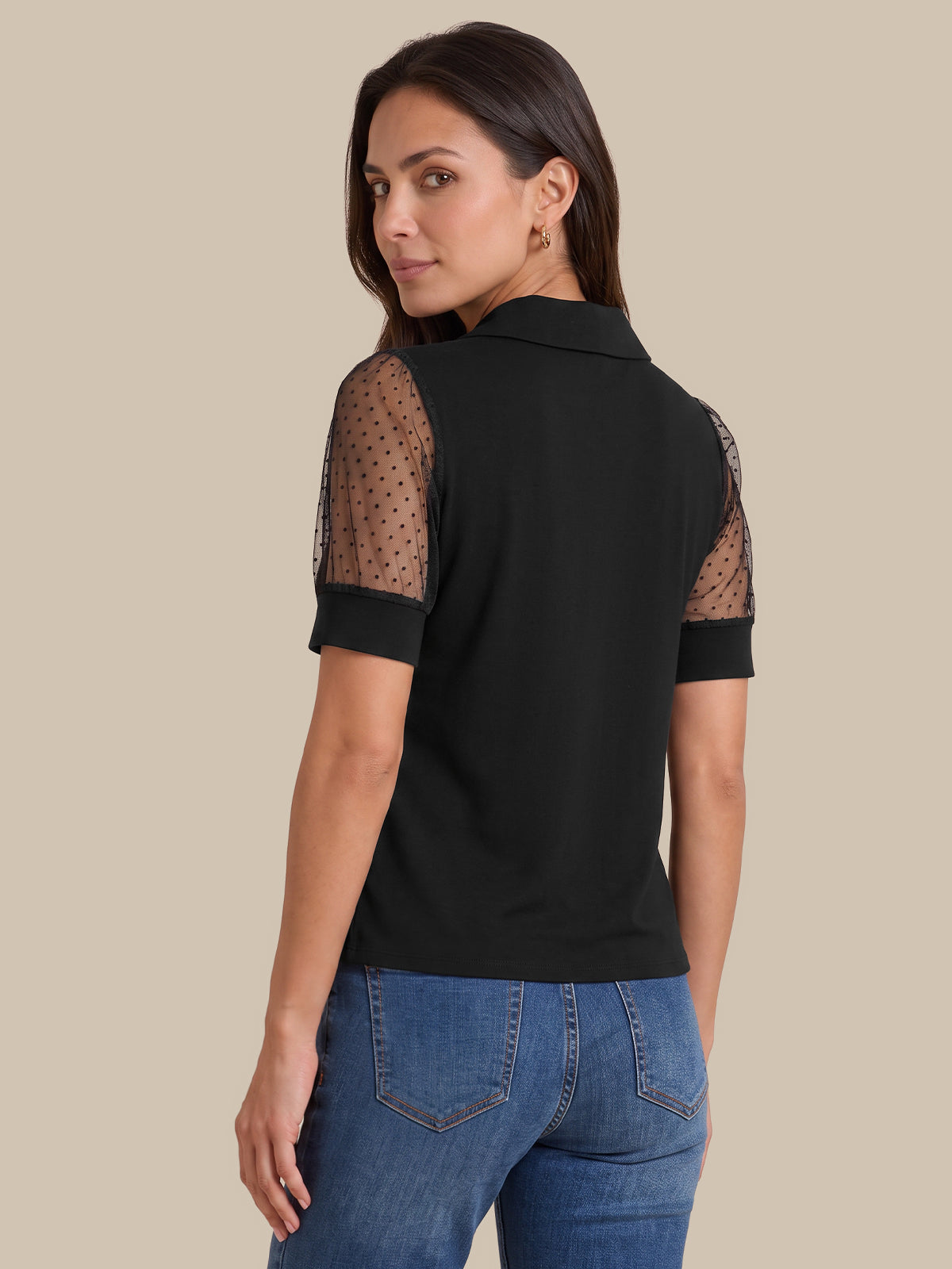A woman shown from the back wearing a black short-sleeve polo shirt with sheer polka-dot mesh sleeves, paired with blue jeans, against a solid beige background.