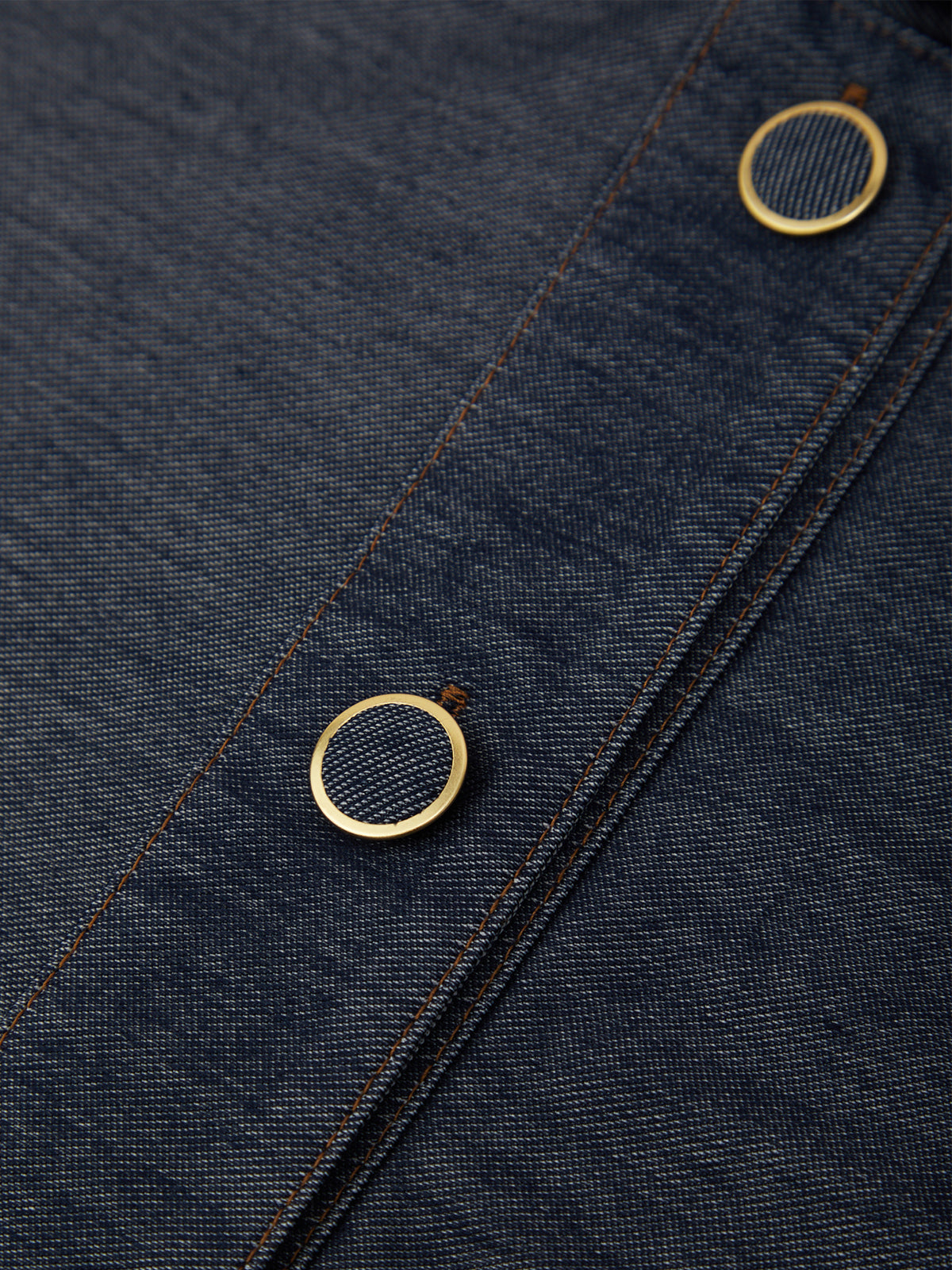 Close-up of dark indigo denim fabric with two round gold-tone metal buttons along a seam.
