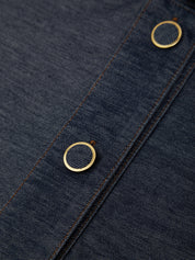 Close-up of dark indigo denim fabric with two round gold-tone metal buttons along a seam.