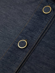 Close-up of dark indigo denim fabric with two round gold-tone metal snap buttons and contrast stitching.