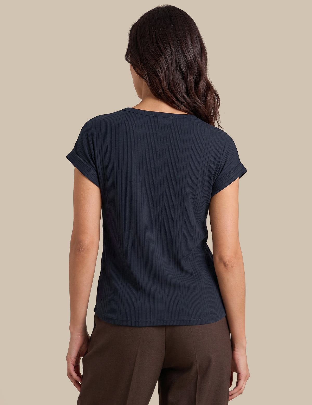A woman shown from the back wearing a dark navy ribbed short-sleeve top and brown pants, set against a solid beige background.
