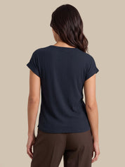A woman shown from the back wearing a dark navy ribbed short-sleeve top and brown pants, set against a solid beige background.