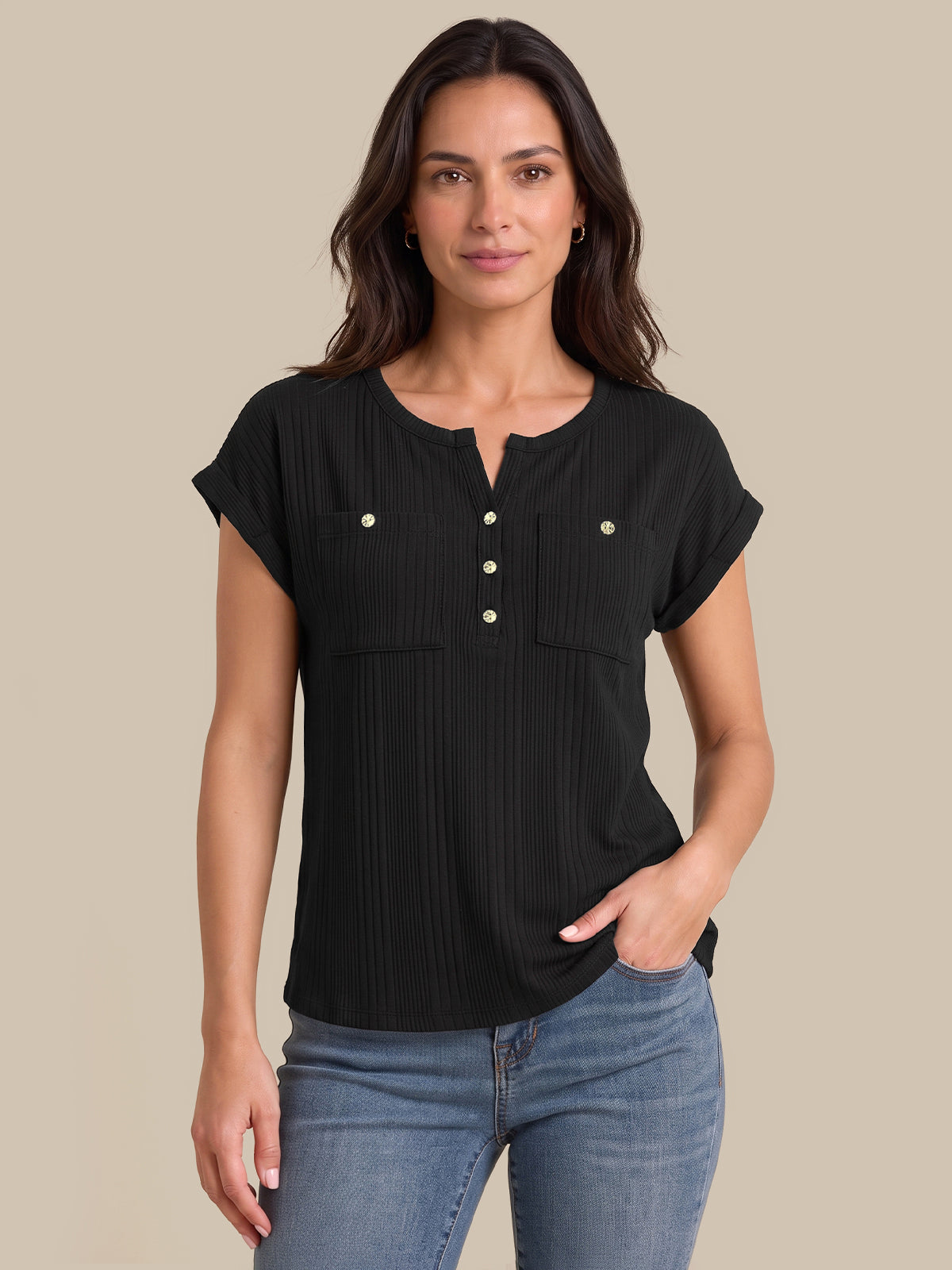 A woman modeling a black short-sleeve ribbed henley top with button details and chest pockets, paired with blue jeans, against a solid beige background.