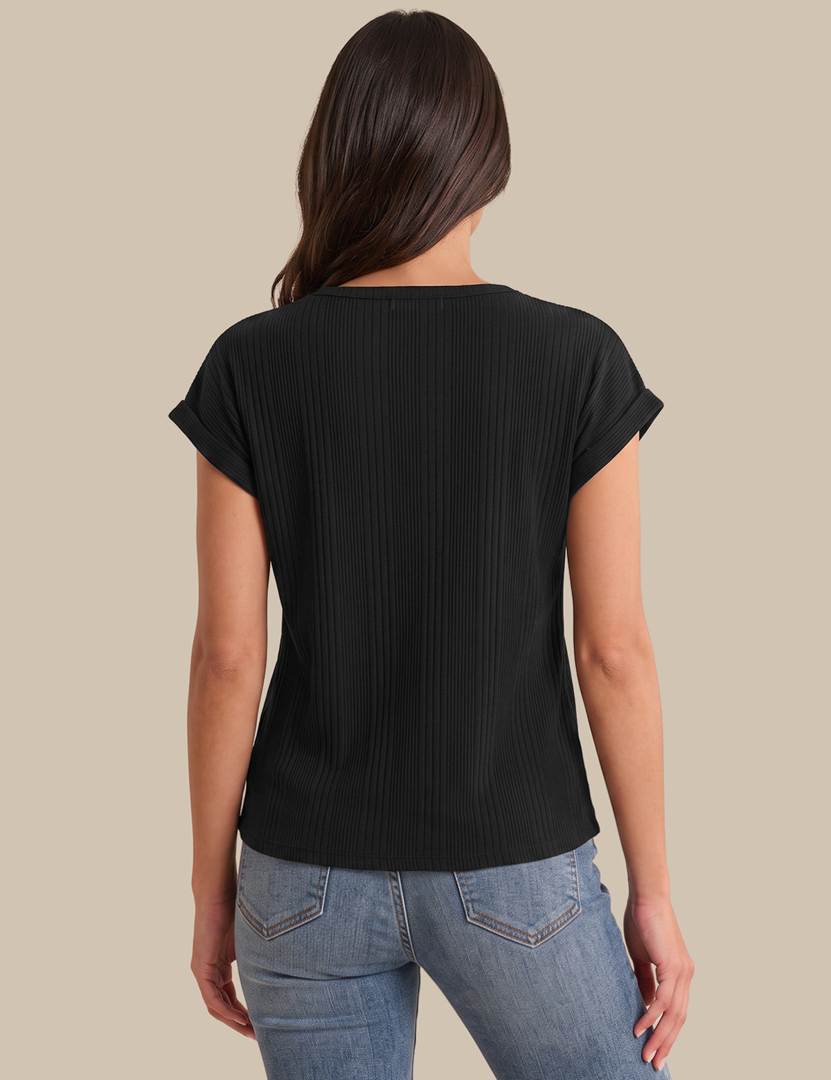 A woman viewed from the back wearing a black short-sleeve ribbed top and light blue jeans against a solid beige background.