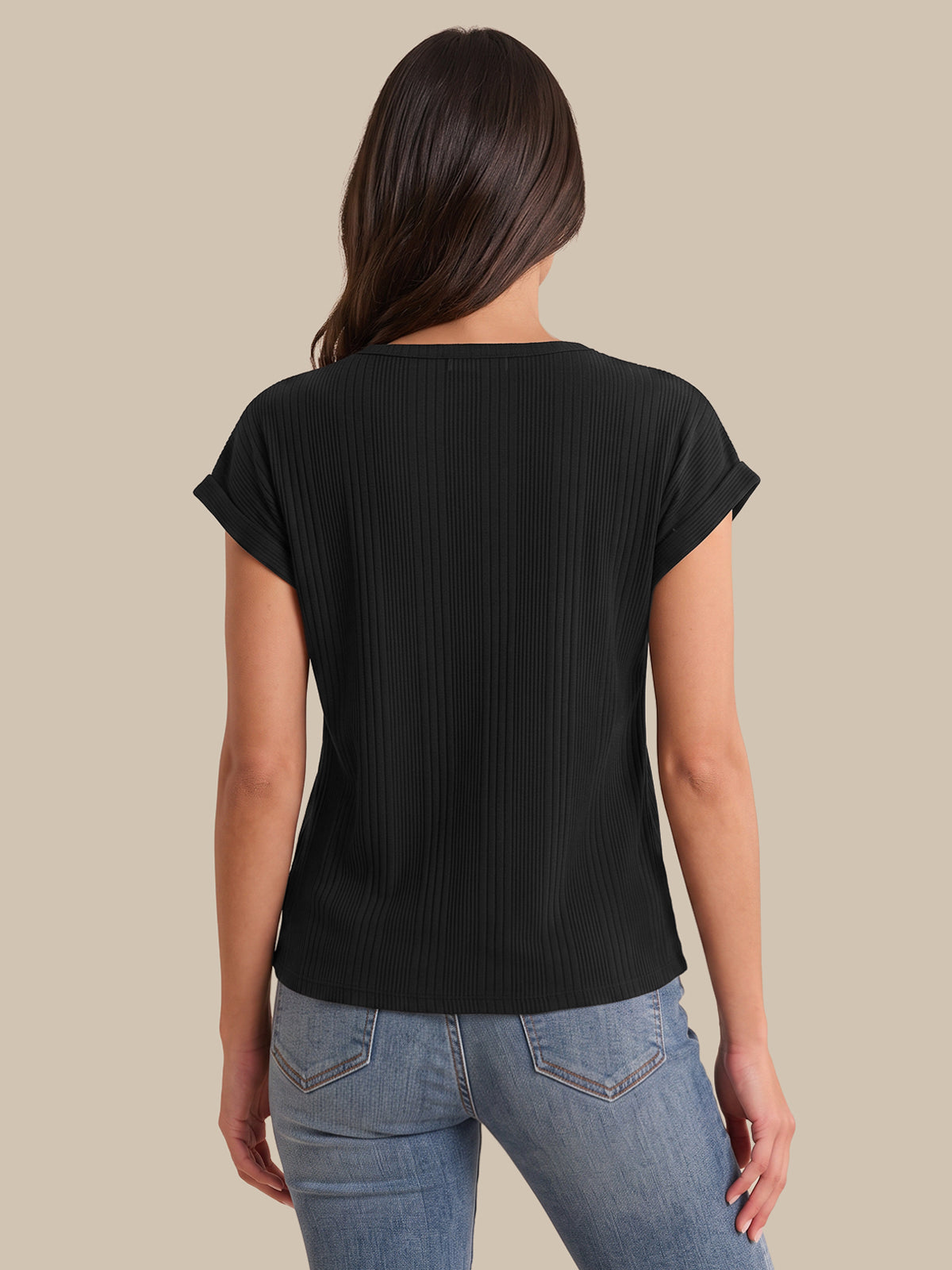 A woman viewed from the back wearing a black short-sleeve ribbed top and light blue jeans against a solid beige background.